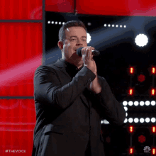 a man in a suit is singing into a microphone while clapping