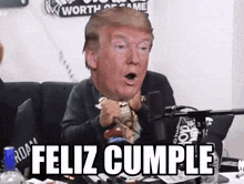 a man sitting in front of a microphone with a donald trump head on his face and the words feliz cumple below him