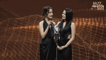 two women standing next to each other in front of a kazz awards poster