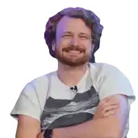 a man with a beard is smiling with his arms crossed and wearing a white shirt with a picture of the ocean on it