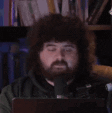 a man with a beard is sitting in front of a microphone with his eyes closed .