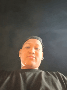 a man wearing a black shirt and a black hat looks at the camera