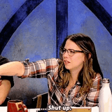 a woman in a plaid shirt is sitting at a table with a man and says shut up