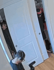 a man wearing headphones is taking a picture of a man in a hat peeking out of a closet .