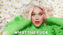 a woman in a green sweater is laying in a pile of daisies and holding her head .