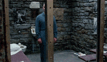 a man in a prison cell with a toilet and a picture on the wall