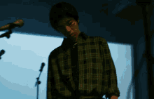 a man in a green plaid shirt is playing a guitar