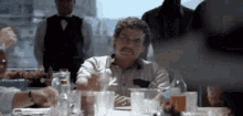 a man with a mustache is sitting at a table with a bunch of glasses of water .