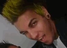 a man with green hair is making a funny face and sticking out his tongue .