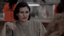 a woman in a prison uniform is giving the middle finger to another woman .