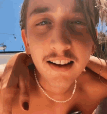 a shirtless man with a pearl necklace around his neck is smiling