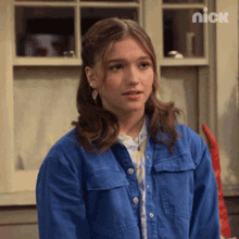a girl wearing a blue denim jacket is standing in front of a window with nick written on the wall behind her