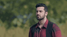 a man with a beard wearing a red plaid shirt and black vest