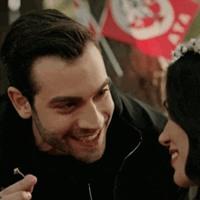 a man and a woman are smiling at each other with a red flag in the background