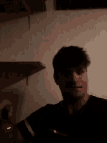 a man in a black shirt is standing in front of a wall in a dark room .