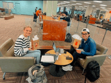 a man and a woman are sitting at a table holding bags of popcorn