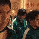 a group of people are standing next to each other in a room wearing green jackets .
