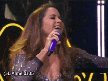 a woman singing into a purple microphone with the hashtag lialmeida05 on the bottom
