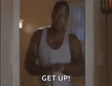 a man in a white tank top is standing in a doorway with his arms crossed .