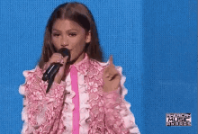 zendaya is wearing a pink jacket and holding a microphone while giving a speech at the american music awards .