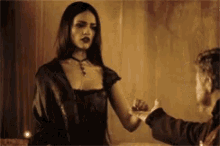 a woman in a black dress is holding a man 's hand in a dark room .
