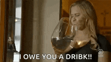 a woman is drinking a glass of wine and saying `` i owe you a drink '' .