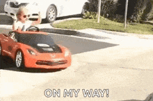 a little boy is driving a red toy car down the street .