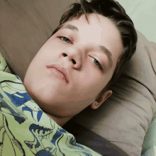 a young boy wearing a dinosaur shirt is laying on a bed