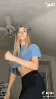 a woman is dancing in a room with a ceiling fan behind her .