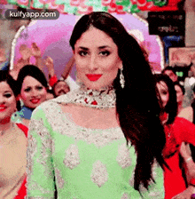 a woman in a green dress is standing in front of a crowd of people and smiling at the camera .