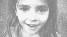 a black and white photo of a little girl making a heart shape with her fingers .