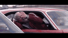 an older man in a red jacket is sitting in a red car