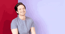 a man in a grey t-shirt is sitting in front of a red and purple wall .