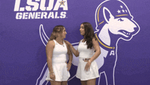 two women standing in front of a lsua generals sign