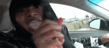 a woman is sitting in the driver 's seat of a car holding a cigarette in her mouth .
