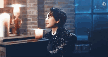 a man in a black jacket is sitting in front of a fireplace with candles .