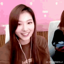 a woman wearing headphones is smiling and looking at the camera while sitting in front of a pink wall .