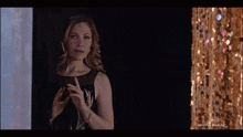 a woman in a black dress is standing in front of a gold sequined wall