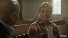 a man in a plaid shirt talks to another man in a church with a netflix logo in the corner