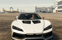 a man is driving a white sports car on a runway with a plane in the background