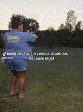a woman in a blue shirt and shorts is standing in a grassy field with trees in the background