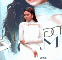 a woman in a white dress stands in front of a sign that says a : k : s