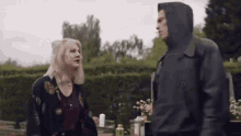 a man in a hooded jacket is standing next to a woman in a floral shirt .