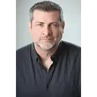 a man with a beard wearing a black shirt is smiling for the camera .