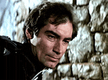 a close up of a man 's face with a stone wall behind him