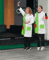 two women in lab coats are dancing on a stage while wearing sneakers .