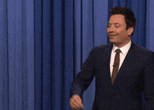 a man in a suit and tie says " rats " in front of a blue curtain