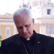 a priest is standing in front of a building wearing a black suit and tie .