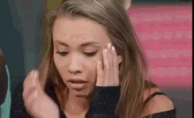 a woman is touching her face with her hands and making a face .