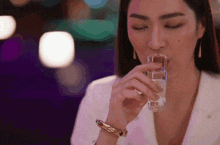 a woman is drinking from a small bottle with her eyes closed